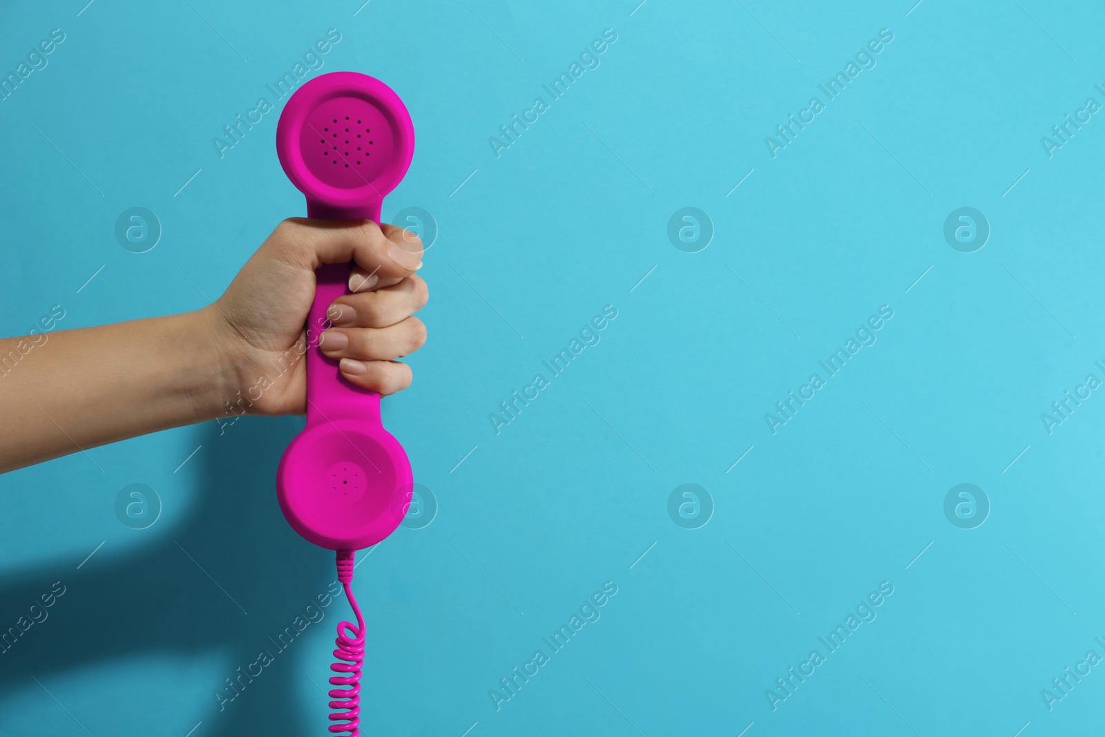 Image of Woman holding magenta telephone handset on light blue background, closeup. Space for text