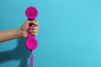 Woman holding magenta telephone handset on light blue background, closeup. Space for text