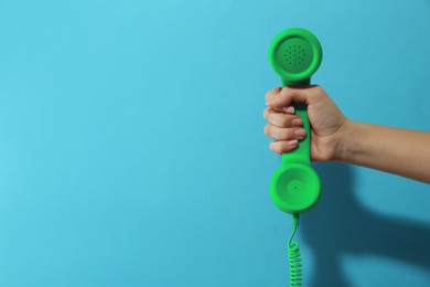 Image of Woman holding green telephone handset on light blue background, closeup. Space for text
