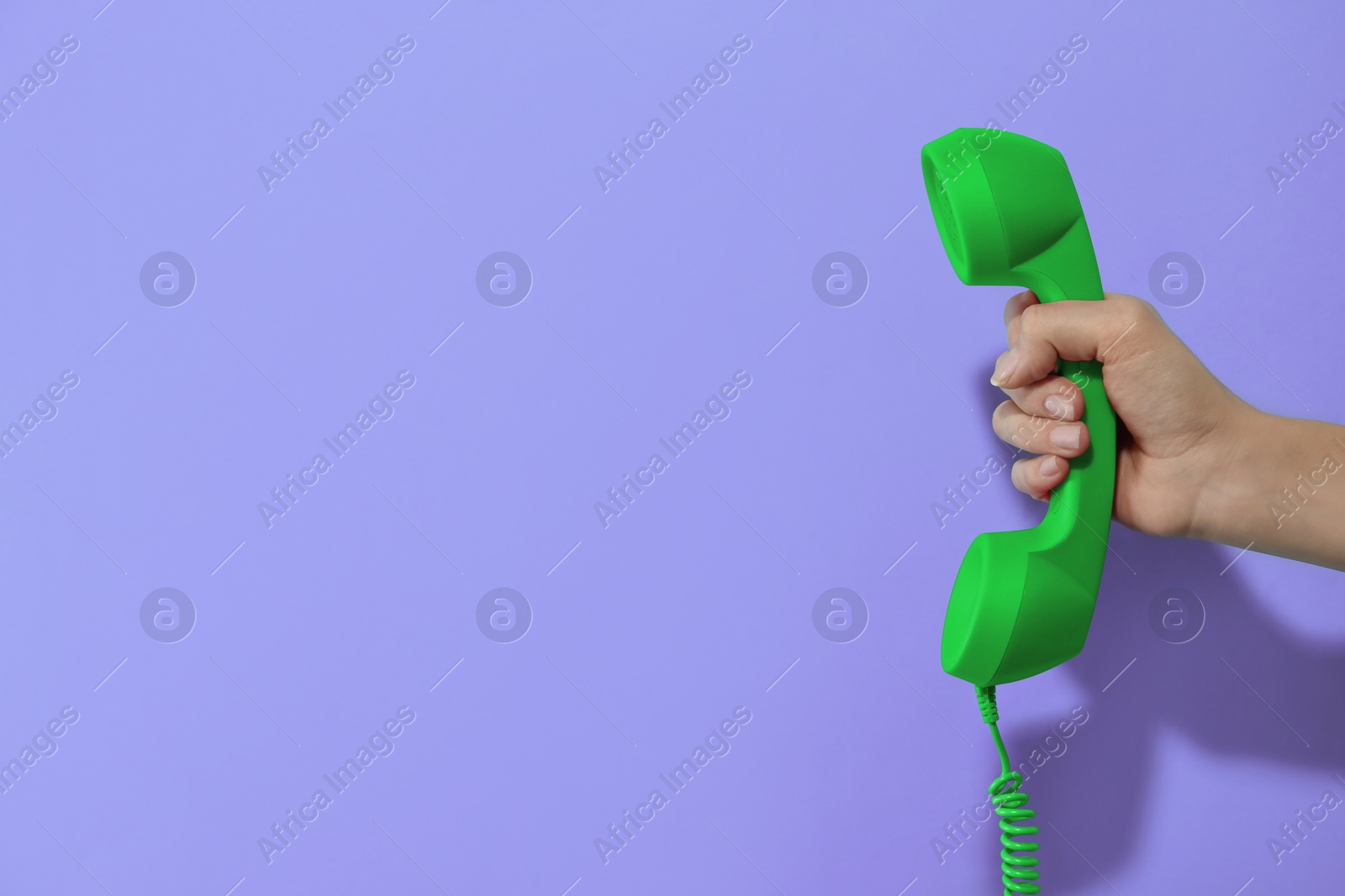 Image of Woman holding green telephone handset on violet background, closeup. Space for text