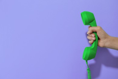 Image of Woman holding green telephone handset on violet background, closeup. Space for text