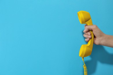 Woman holding yellow telephone handset on light blue background, closeup. Space for text