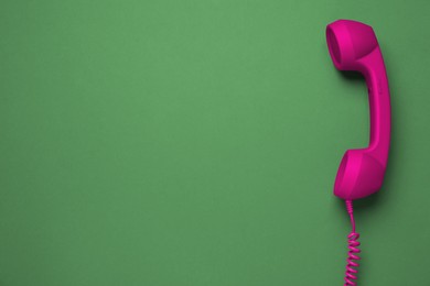 Magenta telephone handset on green background, top view. Space for text