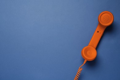 Orange telephone handset on blue background, top view. Space for text