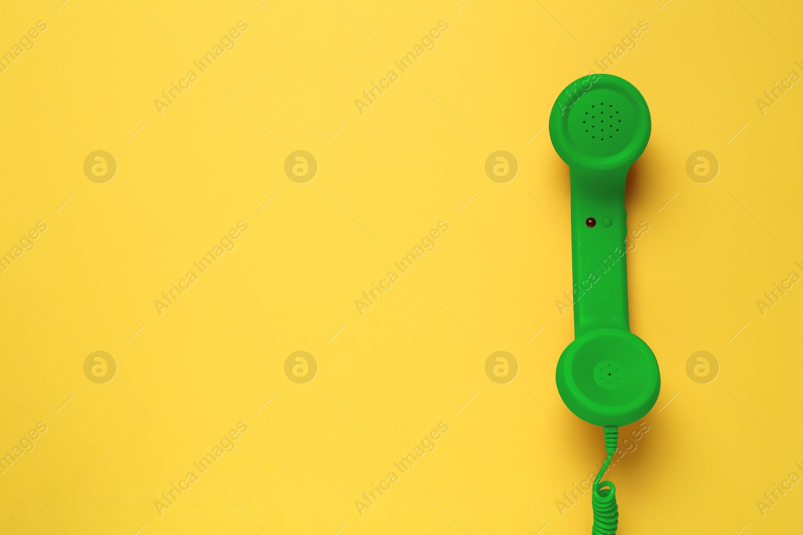 Image of Green telephone handset on yellow background, top view. Space for text