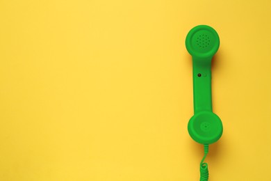 Image of Green telephone handset on yellow background, top view. Space for text