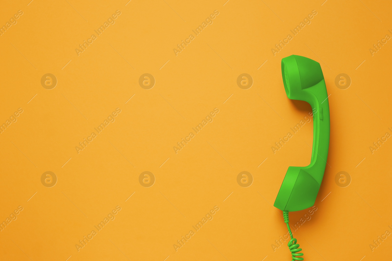 Image of Green telephone handset on orange background, top view. Space for text