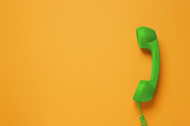 Image of Green telephone handset on orange background, top view. Space for text