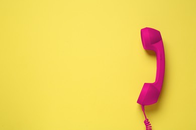 Image of Magenta telephone handset on yellow background, top view. Space for text