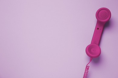 Magenta telephone handset on pink background, top view. Space for text