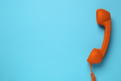 Orange telephone handset on light blue background, top view. Space for text