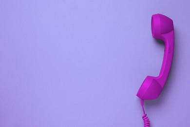 Purple telephone handset on violet background, top view. Space for text