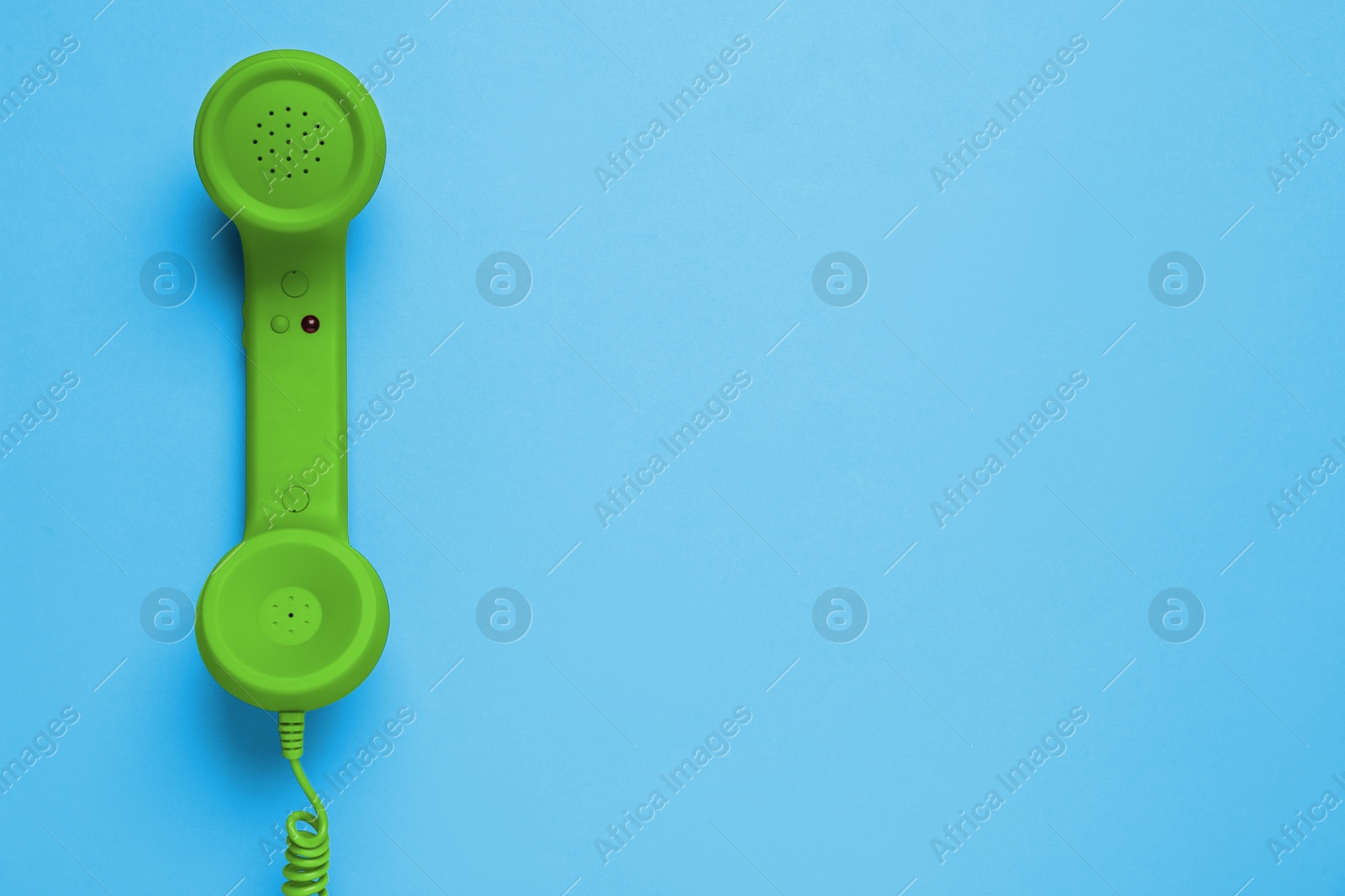 Image of Green telephone handset on light blue background, top view. Space for text