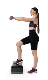 Young woman doing aerobic exercise with dumbbells and step platform on white background