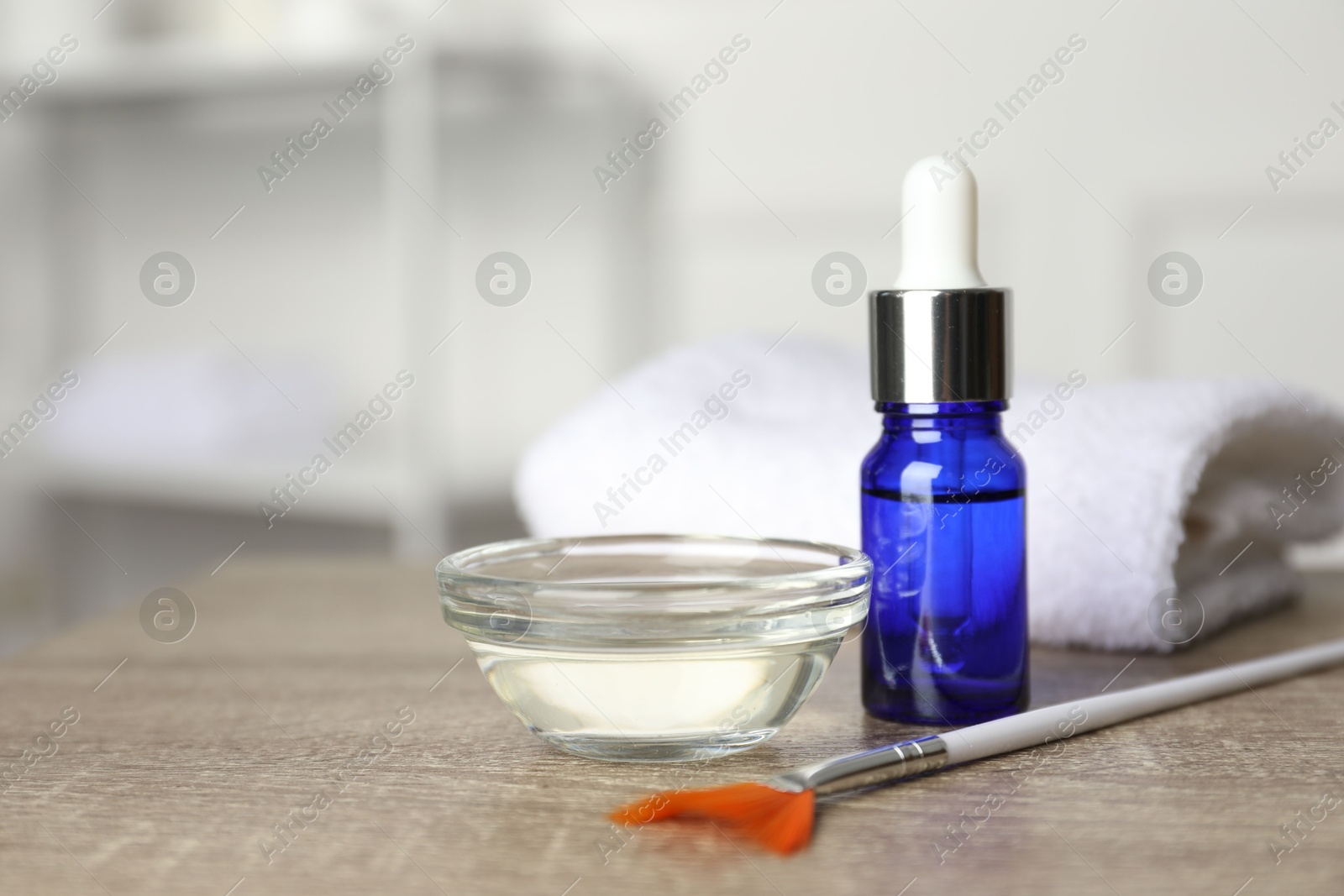 Photo of Peeling procedure. Bottle of chemical peel, bowl with liquid, brush and towel on wooden table indoors