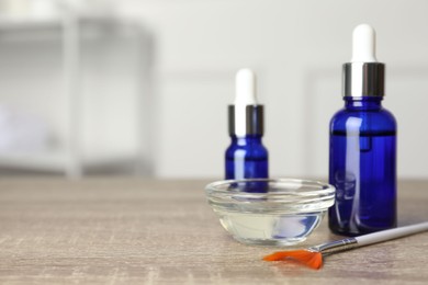 Photo of Peeling procedure. Bottles of chemical peel, bowl with liquid and brush on wooden table indoors. Space for text