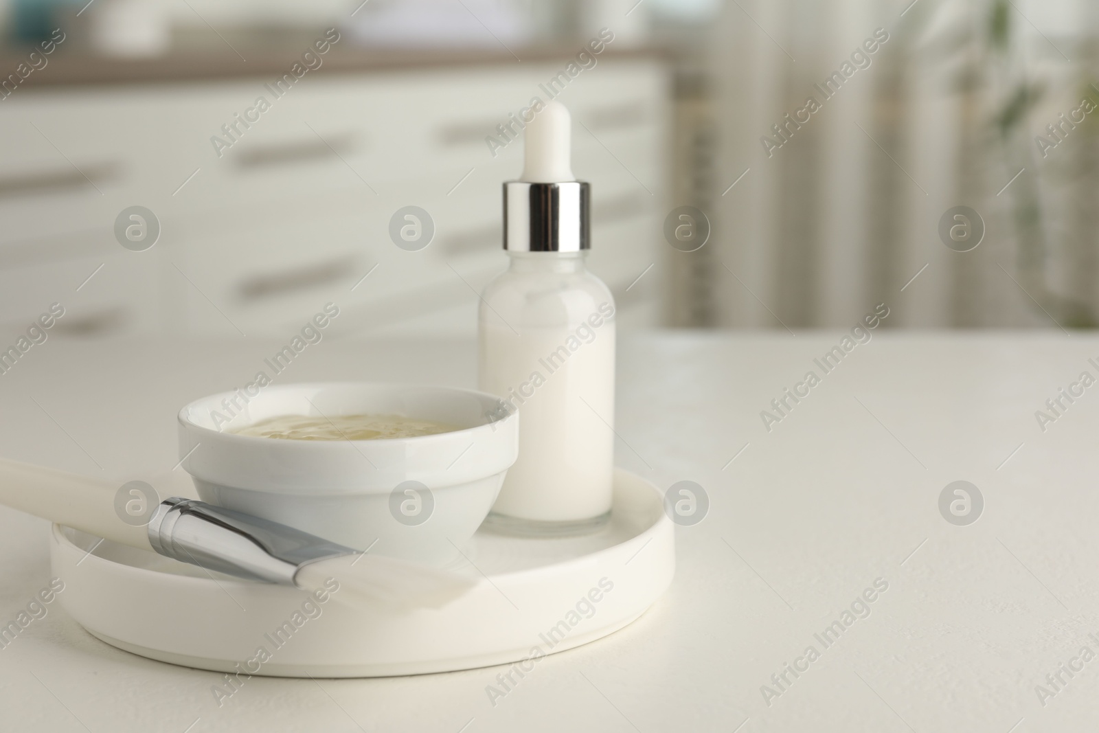 Photo of Peeling procedure. Bottle of chemical peel, bowl with liquid and brush on white table indoors. Space for text