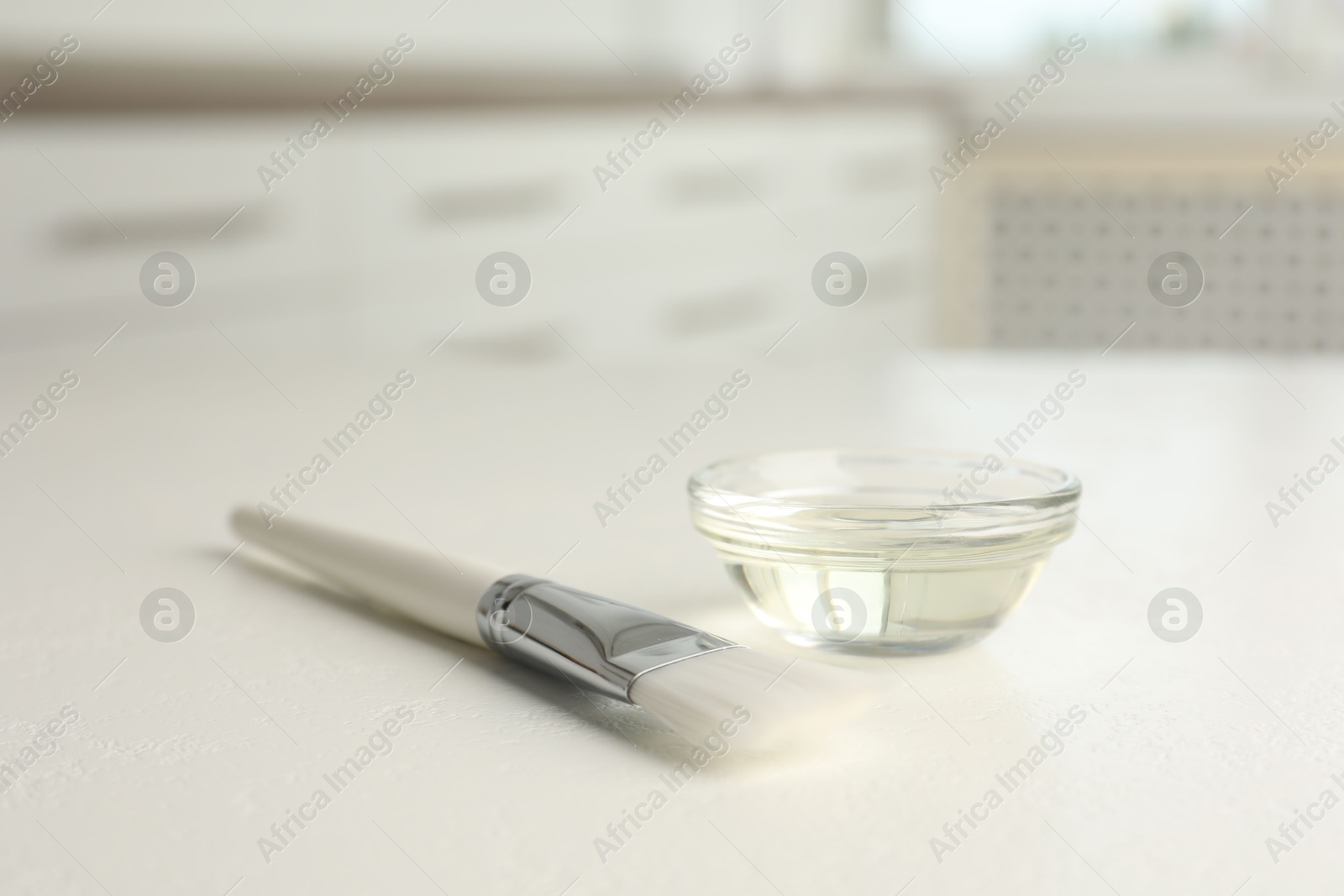 Photo of Peeling procedure. Chemical peel liquid in bowl and brush on white table indoors. Space for text