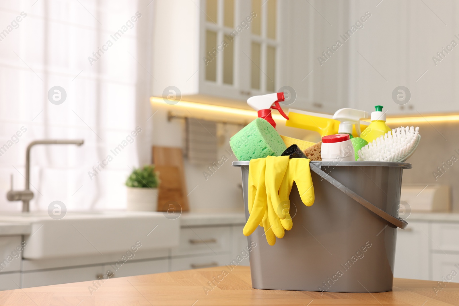 Photo of Cleaning service. Bucket with supplies on table in kitchen. Space for text