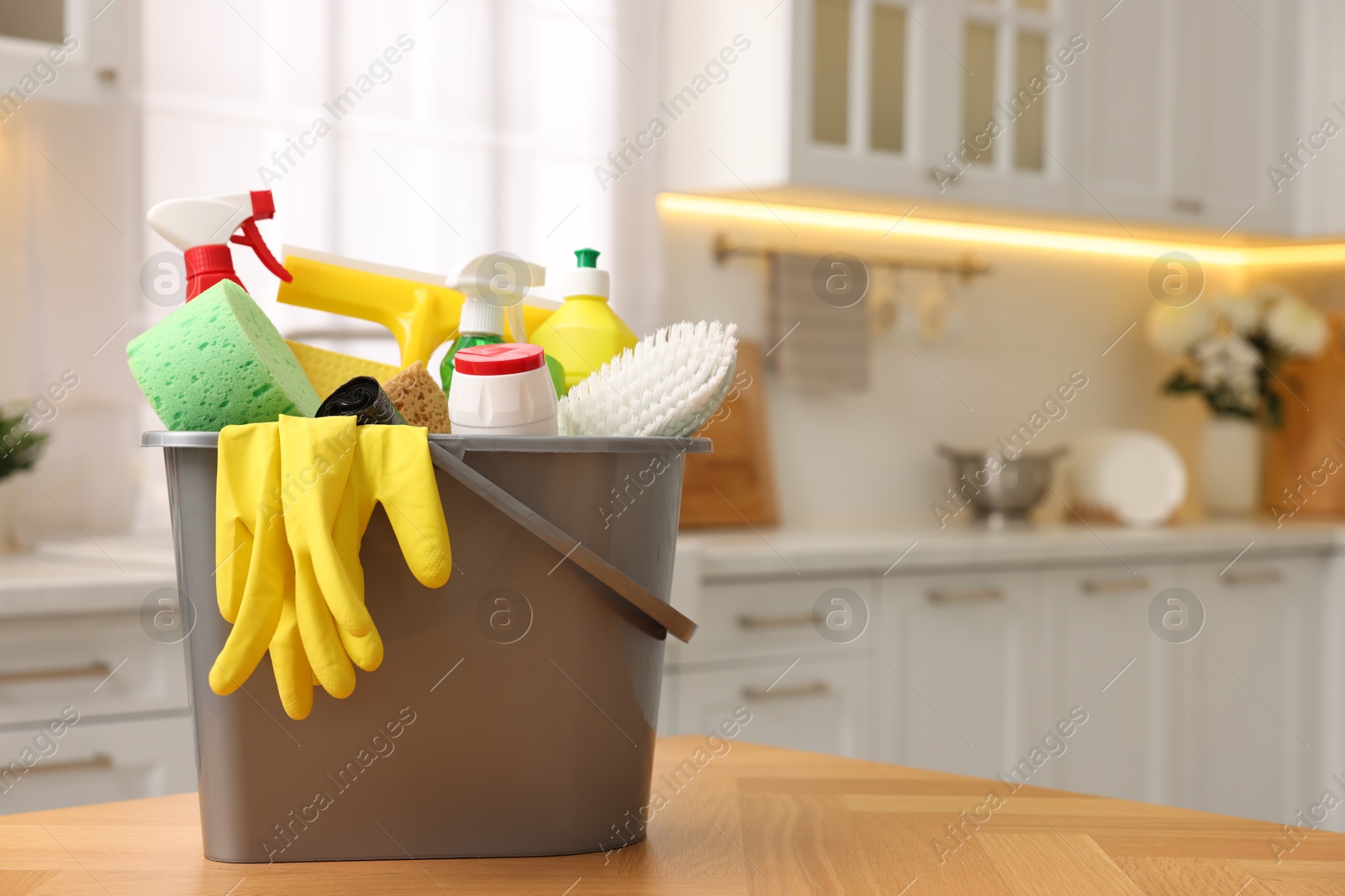 Photo of Cleaning service. Bucket with supplies on table in kitchen. Space for text