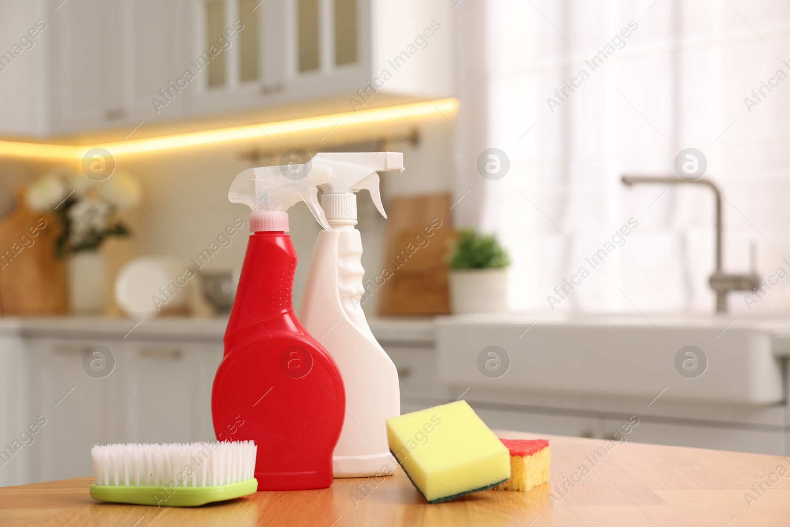 Photo of Cleaning service. Detergents, sponges and brush on table in kitchen. Space for text