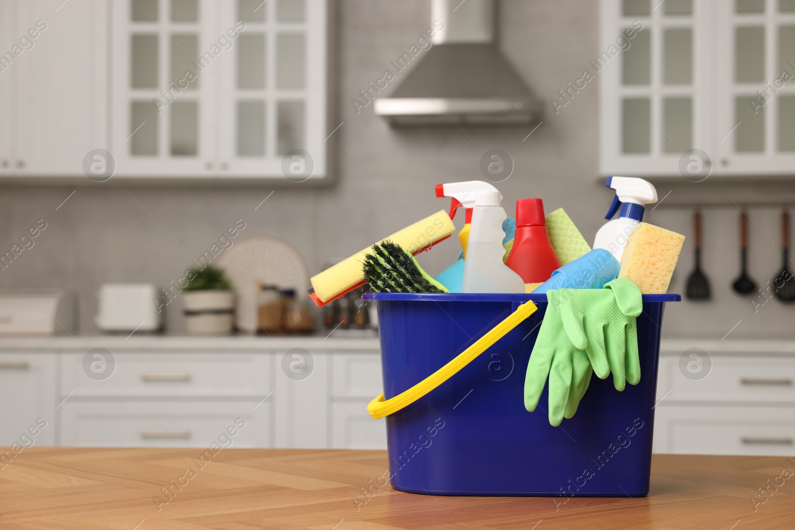 Photo of Cleaning service. Bucket with supplies on table in kitchen. Space for text