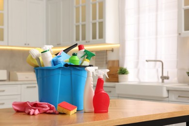 Photo of Cleaning service. Bucket with supplies on table in kitchen. Space for text