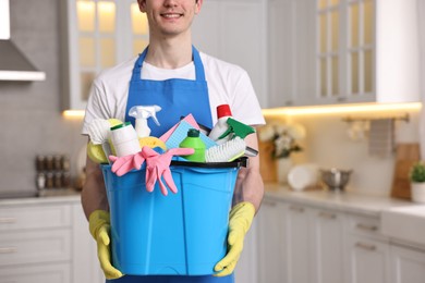 Photo of Cleaning service worker holding bucket with supplies in kitchen, closeup. Space for text