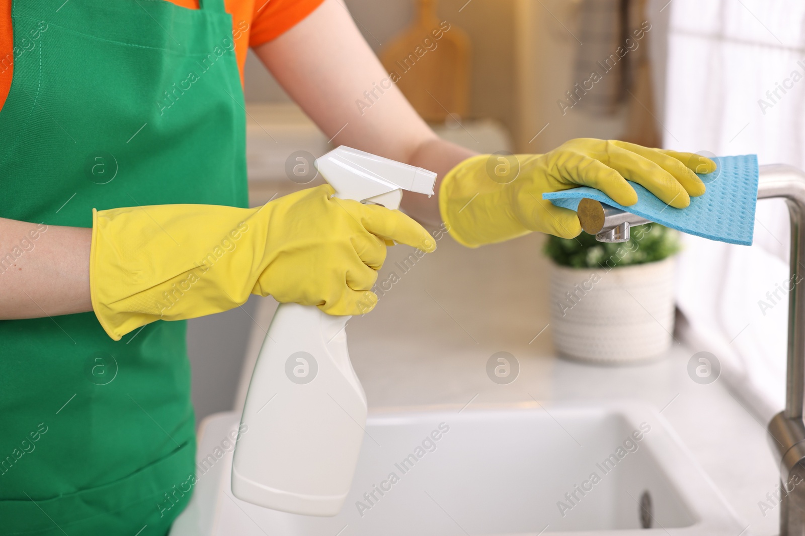 Photo of Professional janitor wearing uniform cleaning tap in kitchen, closeup