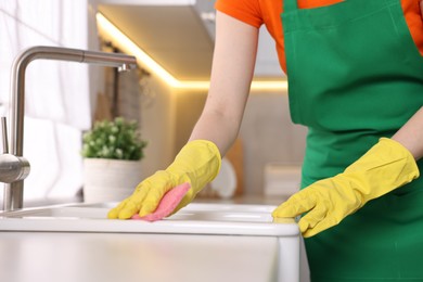Professional janitor wearing uniform cleaning sink in kitchen, closeup
