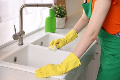 Professional janitor wearing uniform cleaning sink in kitchen, closeup