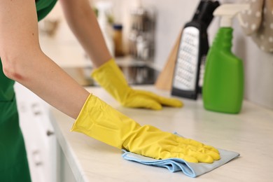 Photo of Professional janitor wearing uniform cleaning countertop in kitchen, closeup