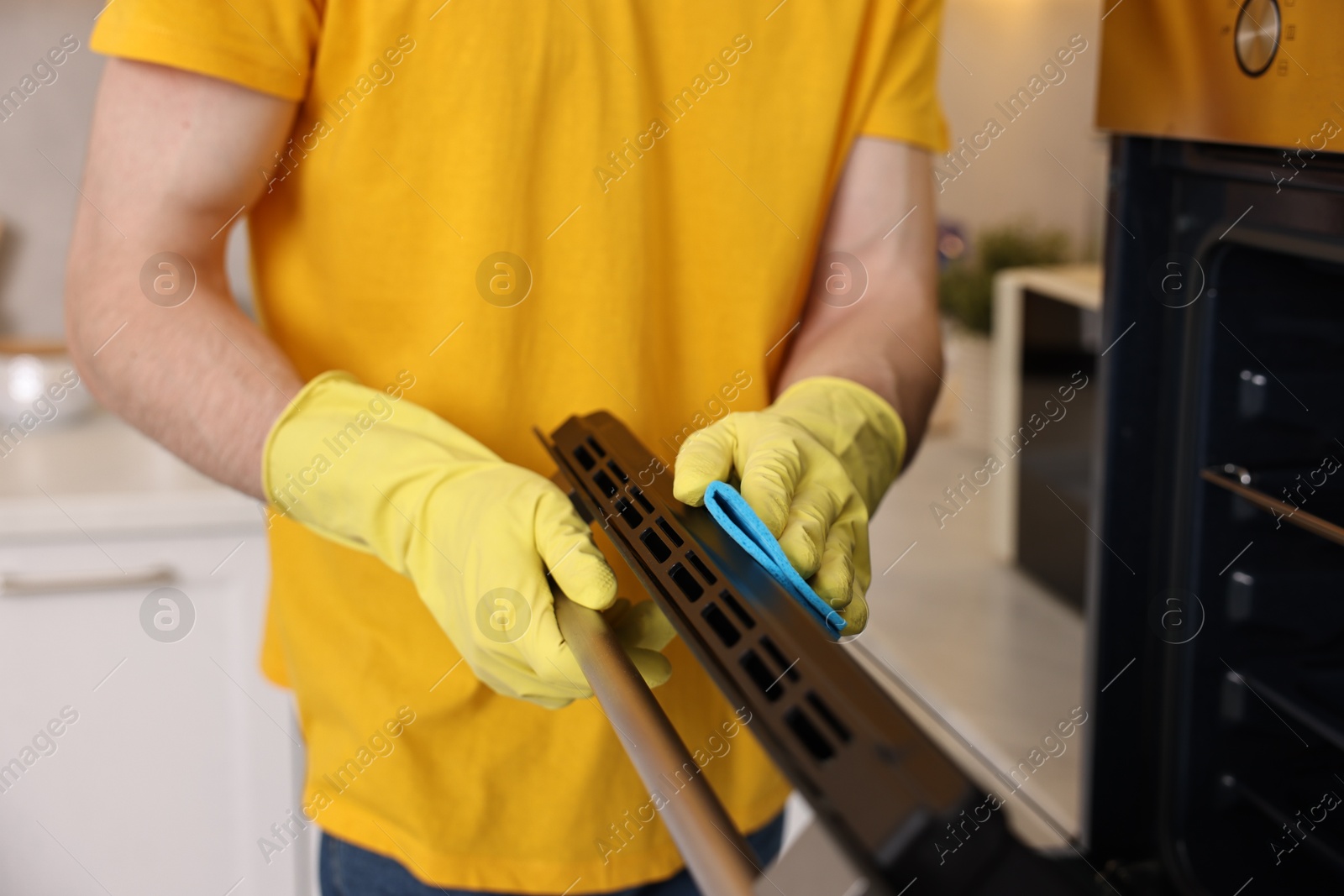 Photo of Professional janitor wearing uniform cleaning electric oven in kitchen, closeup