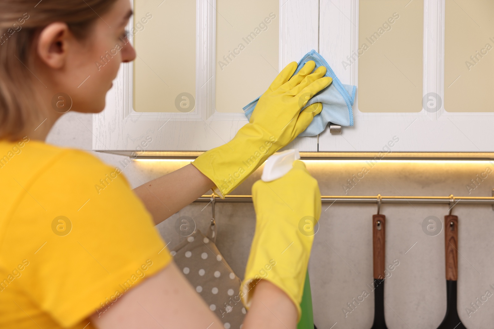 Photo of Professional janitor wearing uniform cleaning cabinet in kitchen, closeup