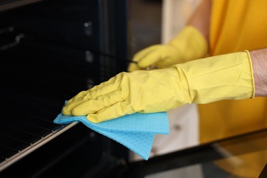 Photo of Professional janitor wearing uniform cleaning electric oven in kitchen, closeup