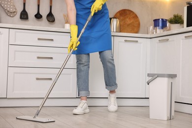 Photo of Cleaning service worker washing floor with mop in kitchen, closeup