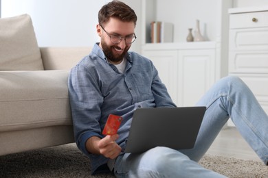Photo of Online banking. Happy young man with credit card and laptop paying purchase at home