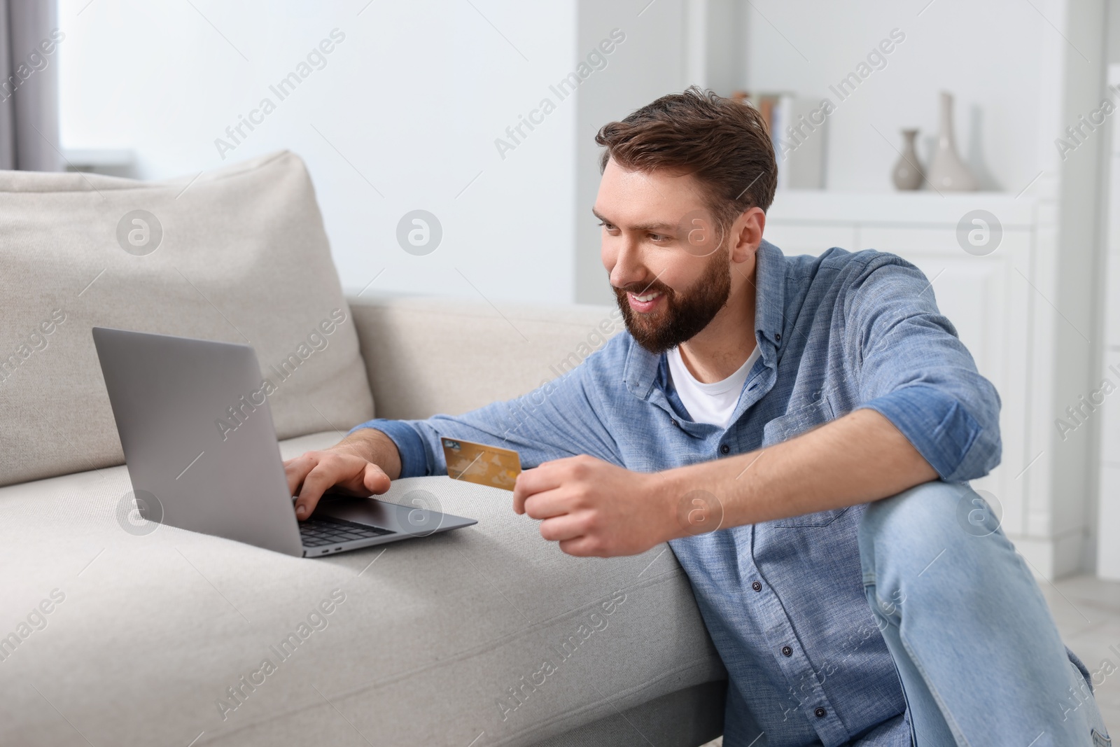 Photo of Online banking. Happy young man with credit card and laptop paying purchase at home