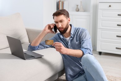 Online banking. Young man with credit card talking by smartphone at home