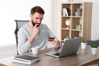 Photo of Online banking. Young man with credit card and laptop paying purchase at table indoors