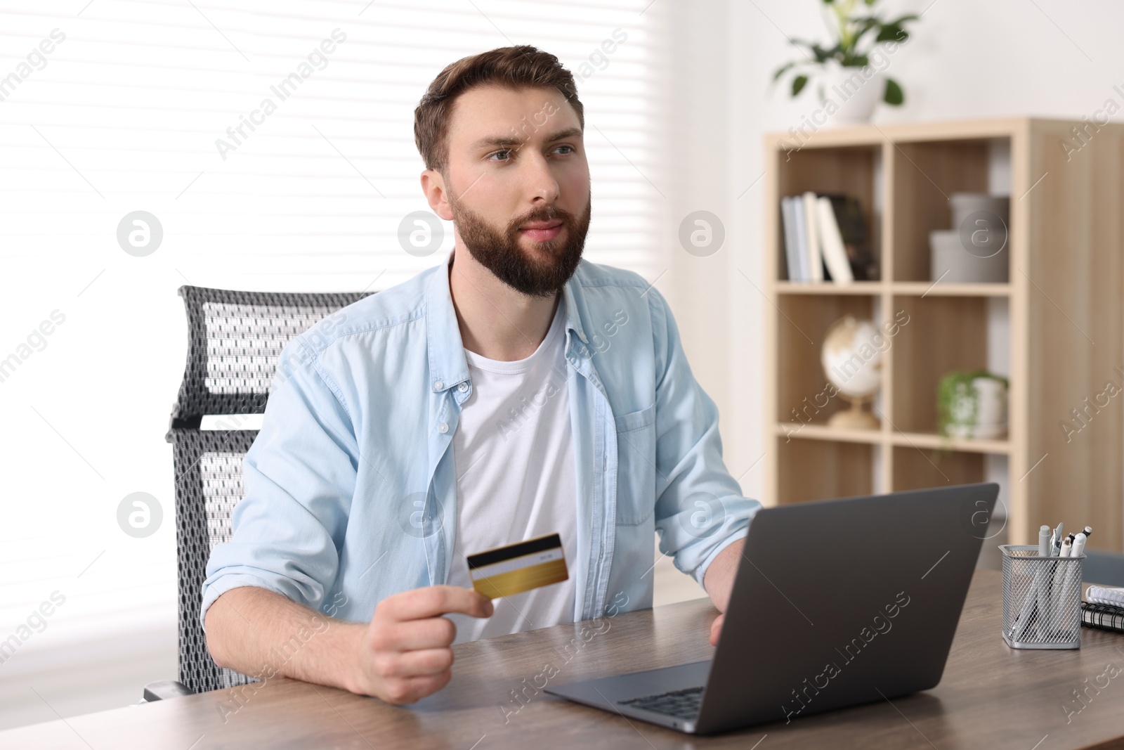 Photo of Online banking. Young man with credit card and laptop paying purchase at table indoors