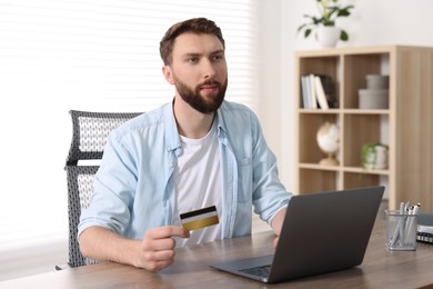 Online banking. Young man with credit card and laptop paying purchase at table indoors