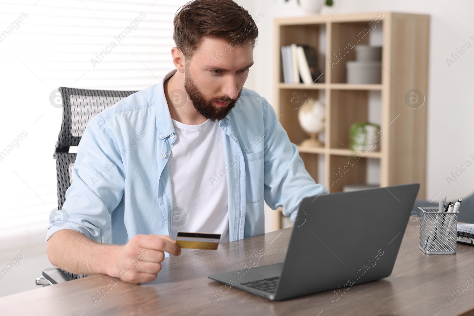 Photo of Online banking. Young man with credit card and laptop paying purchase at table indoors