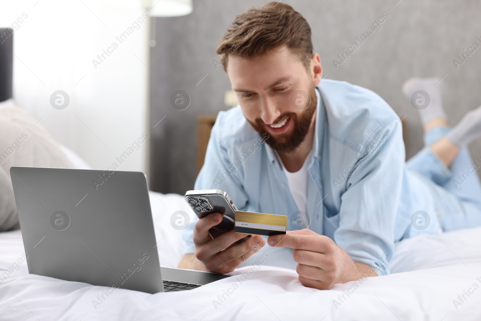 Photo of Online banking. Happy young man with credit card and laptop paying purchase at home