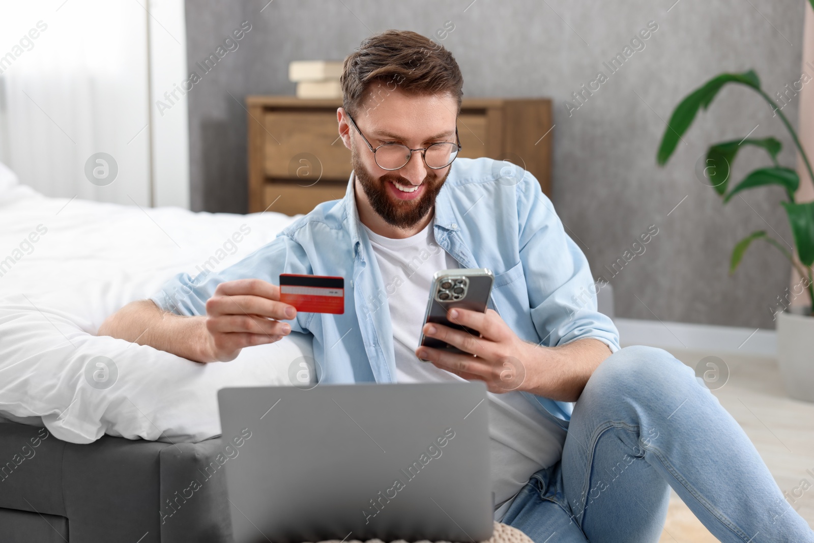 Photo of Online banking. Happy young man with credit card and laptop paying purchase at home