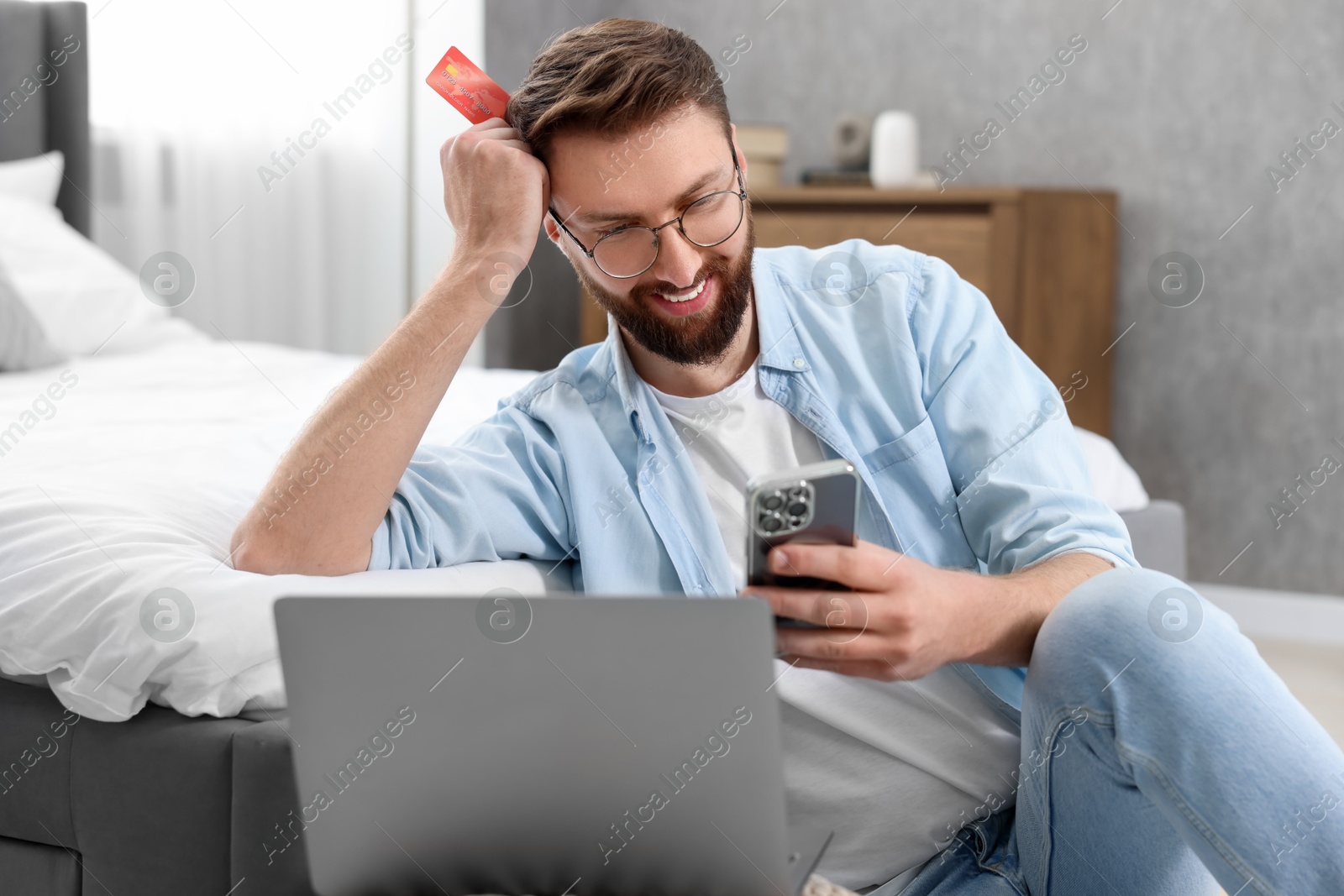 Photo of Online banking. Happy young man with credit card and laptop paying purchase at home