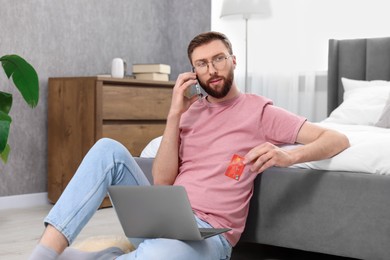 Online banking. Young man with credit card talking by smartphone at home