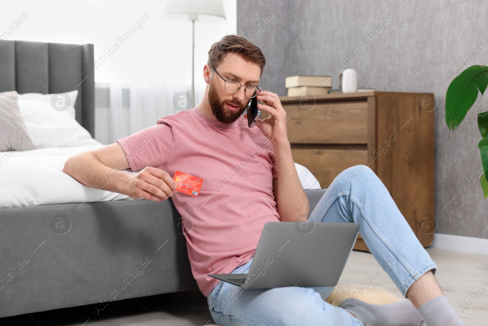 Photo of Online banking. Young man with credit card talking by smartphone at home