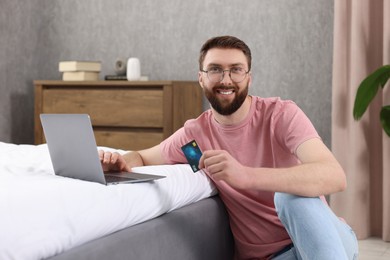 Photo of Online banking. Happy young man with credit card and laptop paying purchase at home