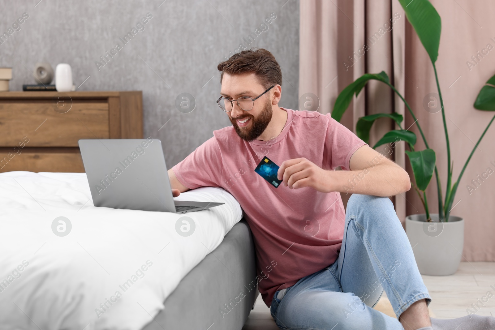 Photo of Online banking. Happy young man with credit card and laptop paying purchase at home